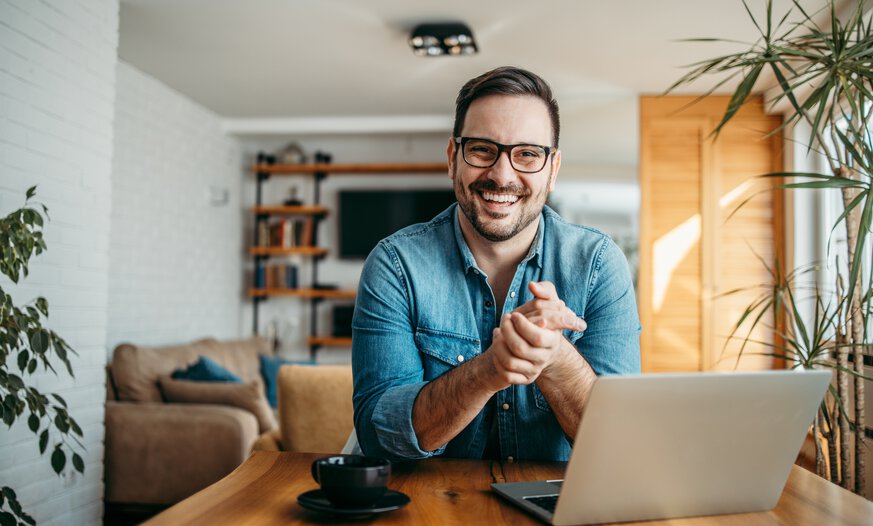 Positive gestimmter Mann sitzt vor geöffnetem Laptop an Schreibtisch