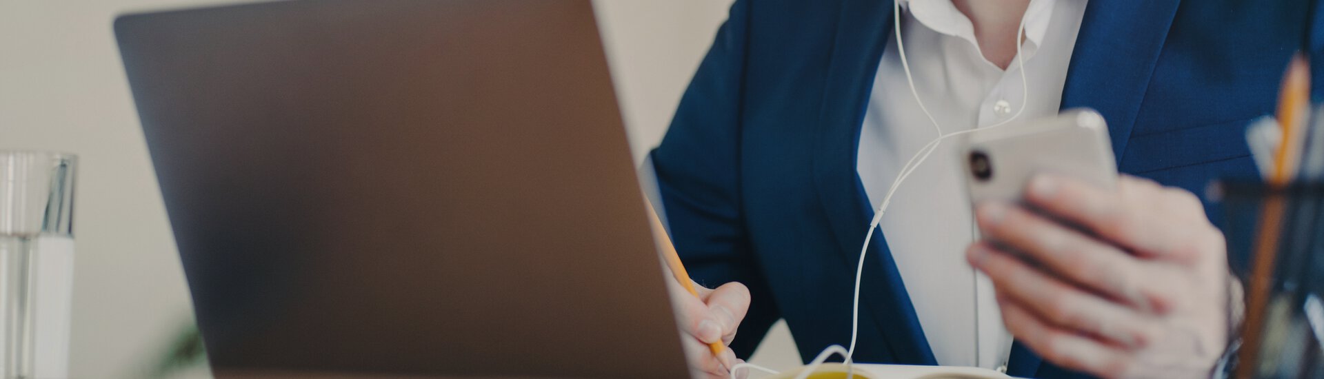 Man vor Laptop mit Handy in der Hand und Kopfhörer im Ohr