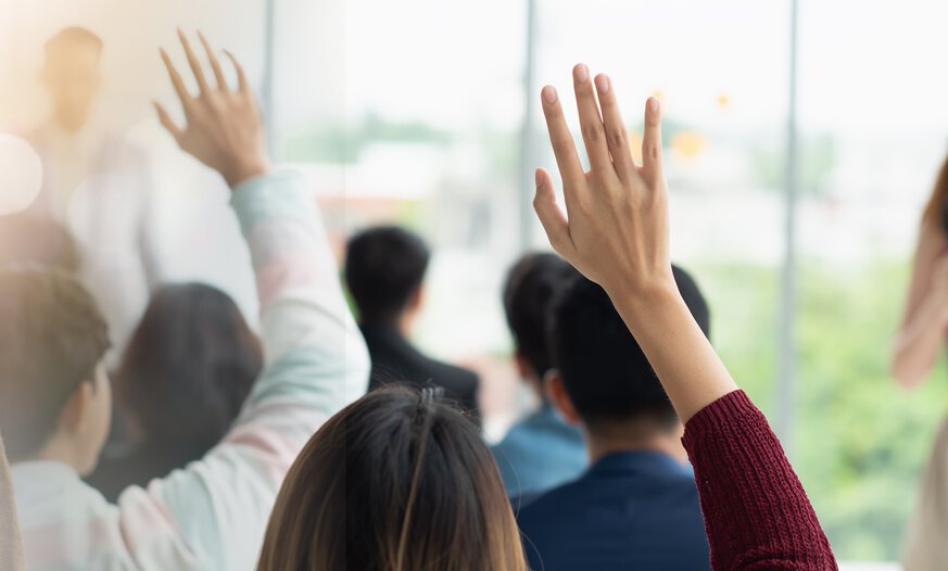 Mehrere Menschen heben die Hand im Unterricht