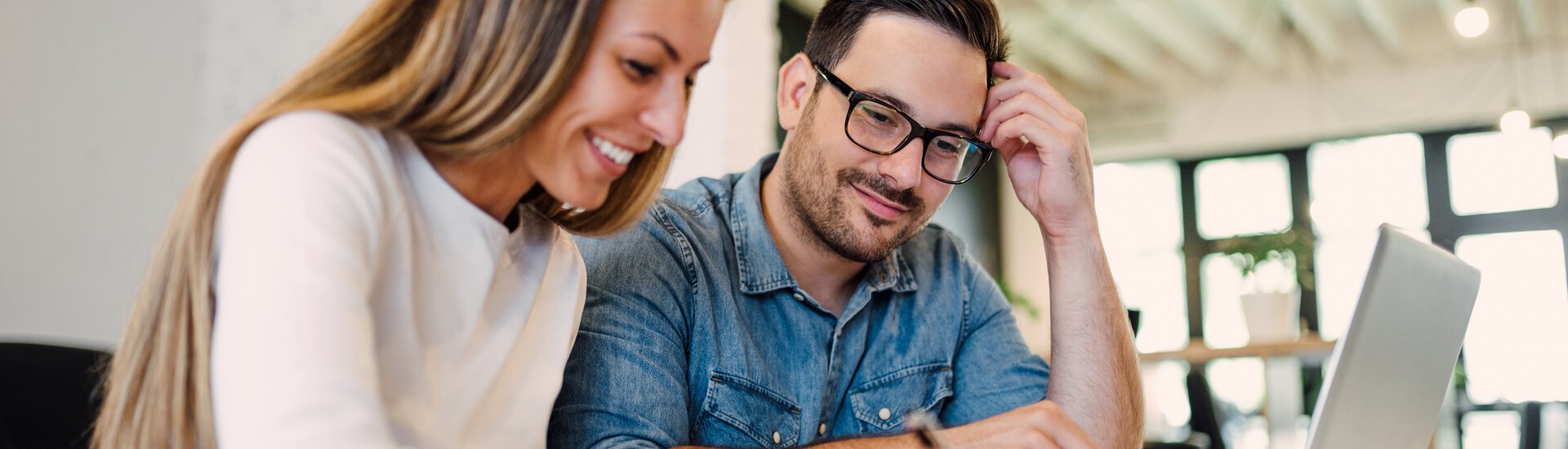 Man und Frau sitzen an einem Laptop Junger Man und junge Frau sitzen lächelnd vor einem Laptop und besprechen etwas angeregt