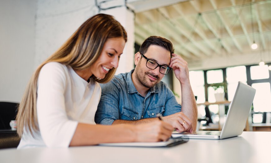 Man und Frau sitzen an einem Laptop Junger Man und junge Frau sitzen lächelnd vor einem Laptop und besprechen etwas angeregt