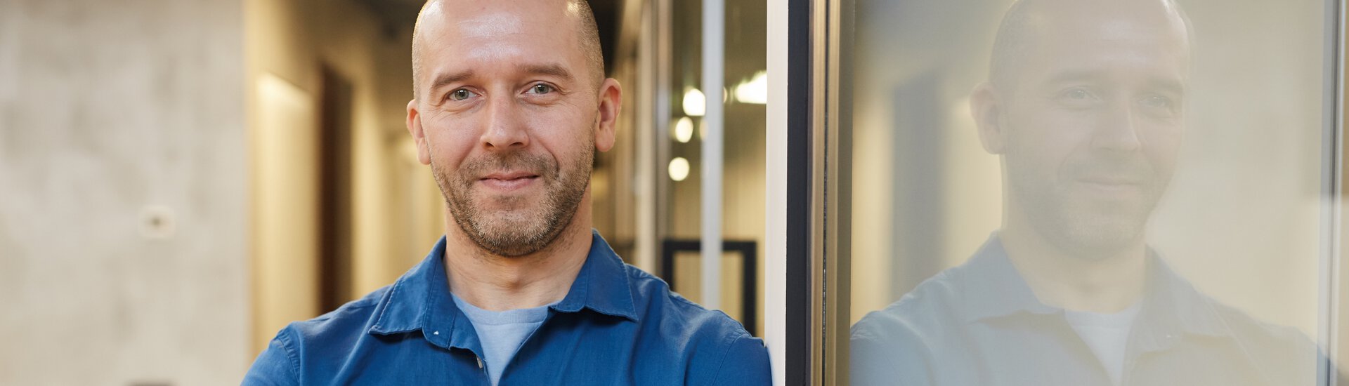 Zuversichtlich gestimmter Mann in dunkelblauem Hemd lehnt an Glaswand
