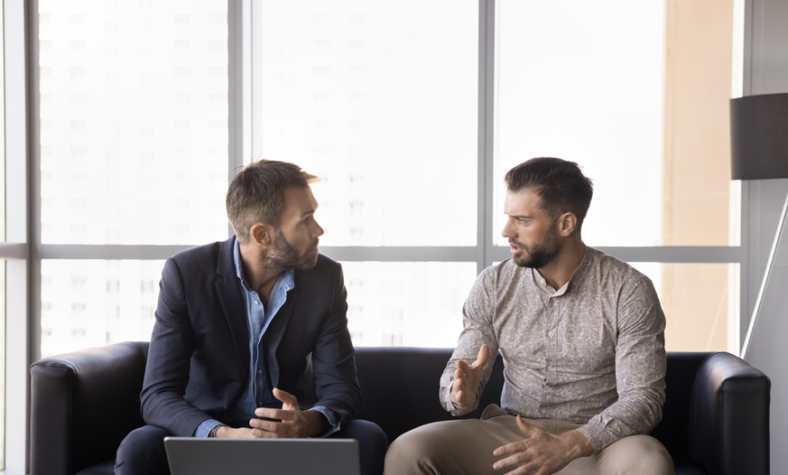 Erste Anlaufstelle: Unsere Berater*innen helfen Ihnen das richtige Angebot zu finden Zwei Männer im Gespräch auf Sofa mit Laptop