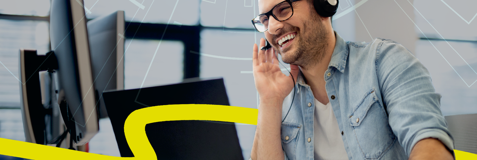 Motivierter Mann mit legerem Jeandshemd und Headset am Schreibtisch mit mehreren Computerbildschirmen