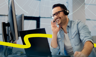 Motivierter Mann mit legerem Jeandshemd und Headset am Schreibtisch mit mehreren Computerbildschirmen
