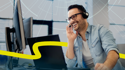 Motivierter Mann mit legerem Jeandshemd und Headset am Schreibtisch mit mehreren Computerbildschirmen