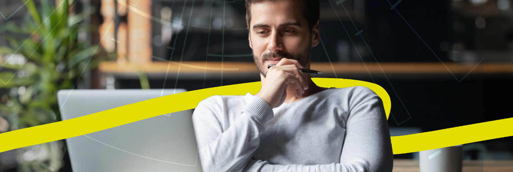 Mann sitzt fokussiert an Schreibtisch und schaut in Laptop