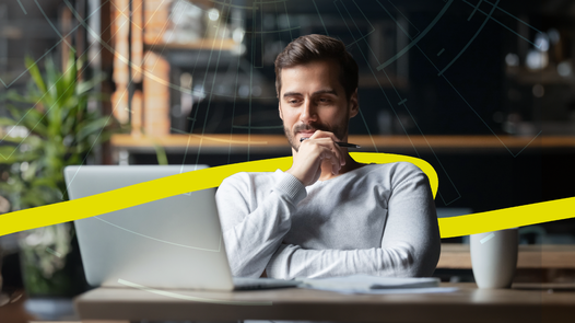 Mann sitzt fokussiert an Schreibtisch und schaut in Laptop