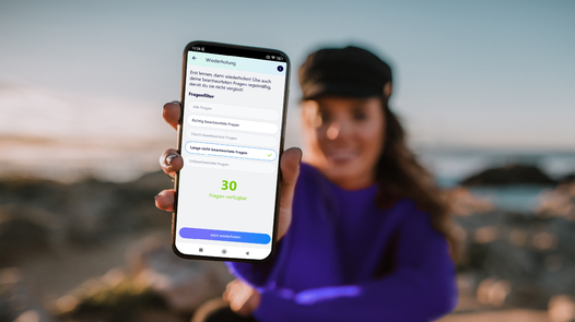 Junge Frau im Hintergrund hält Smartphone mit Führerschein Lern App nach vorne